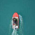 Top view of a red motorboat with fishermen navigating open turquoise waters.